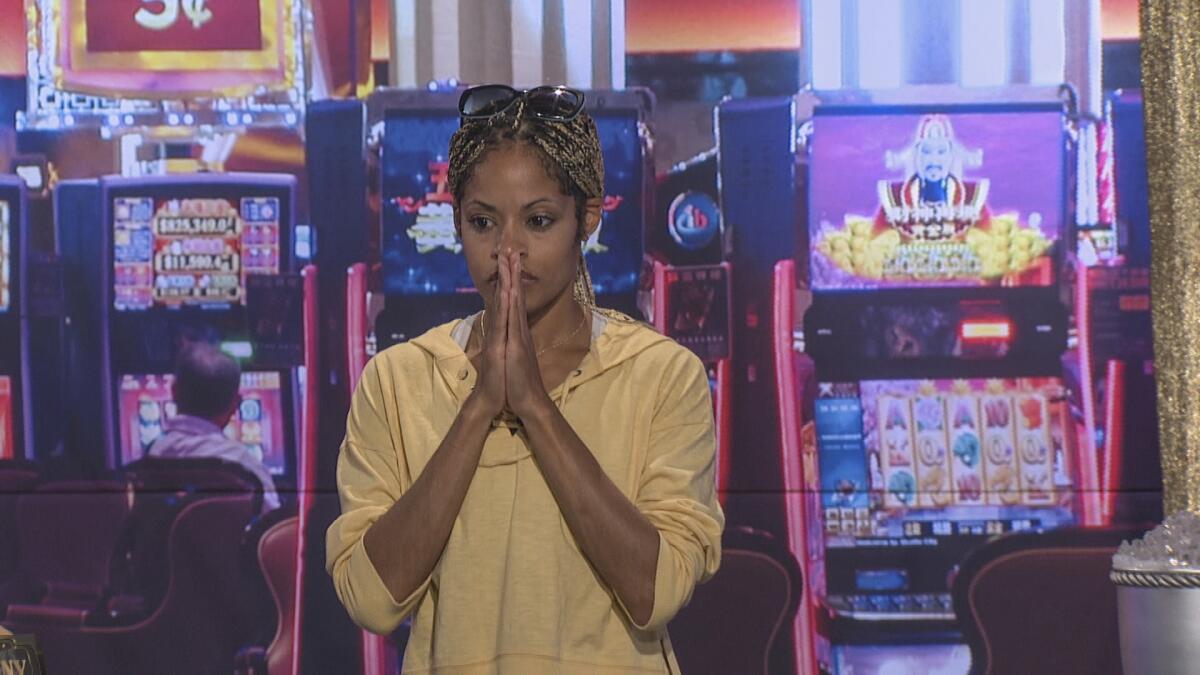 A woman stands with her hands in a prayer shape in front of her mouth, before a casino backdrop