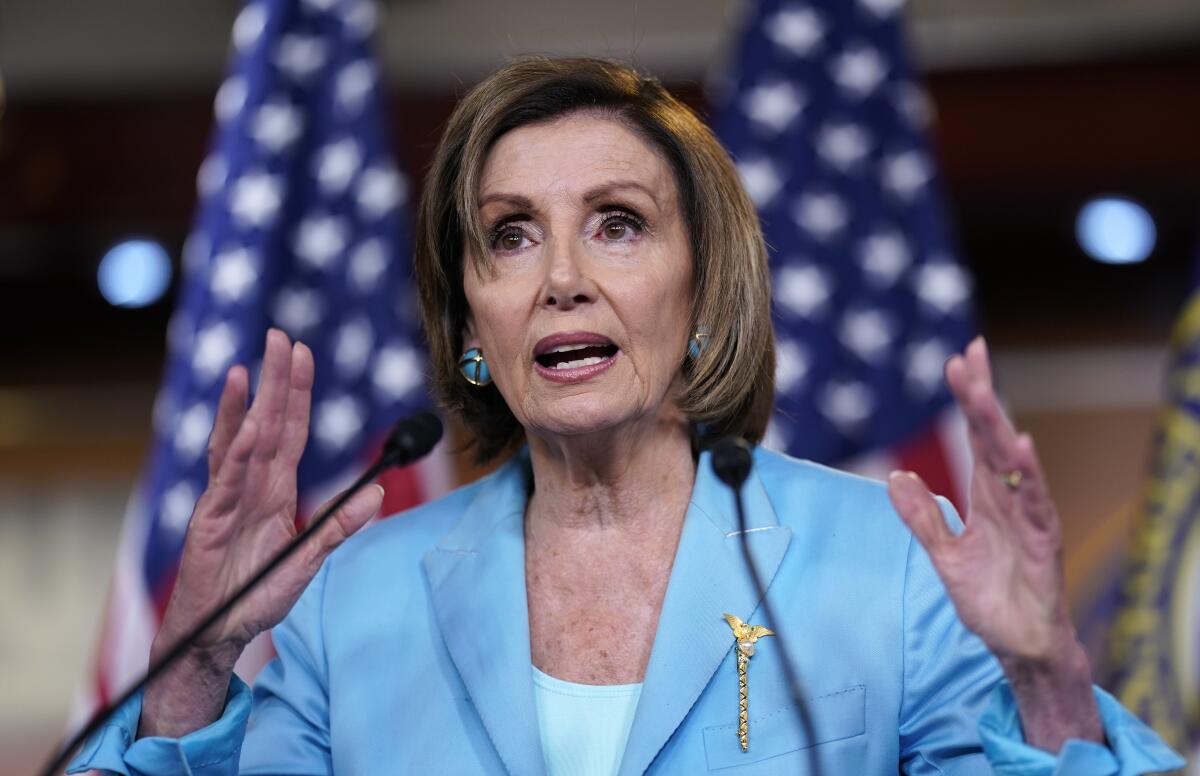 Speaker of the House Nancy Pelosi talks at a microphone with her hands up on either side of her.