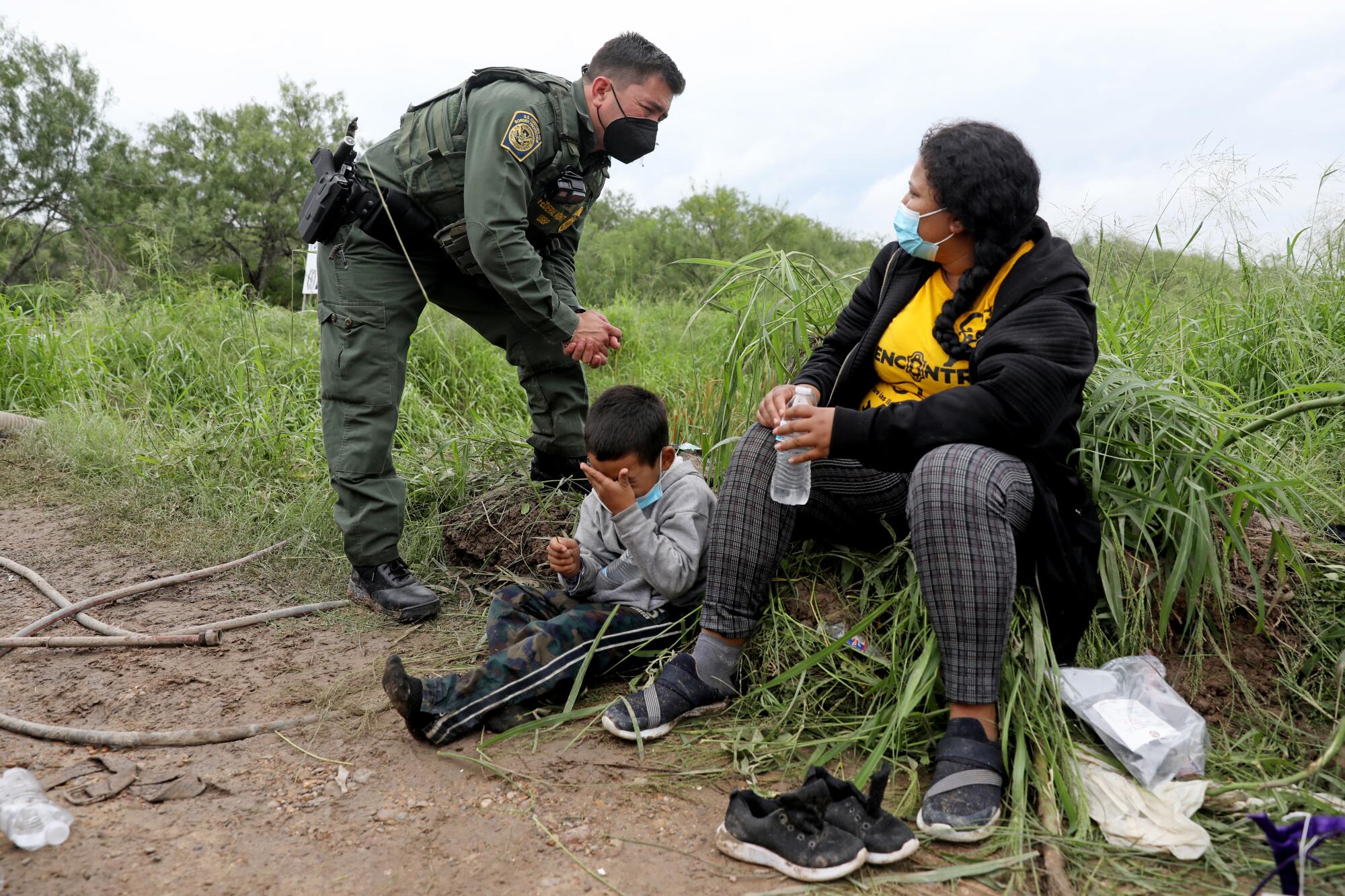 An agent in uniform, left, speaks with a woman seated next to a child 