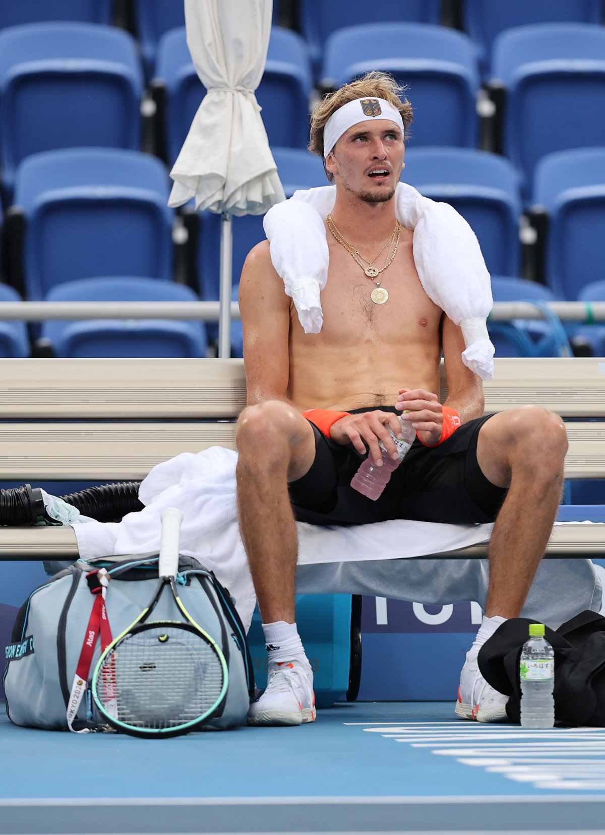 Alexander Zverev, seated and shirtless, has an ice pack draped around his shoulders.