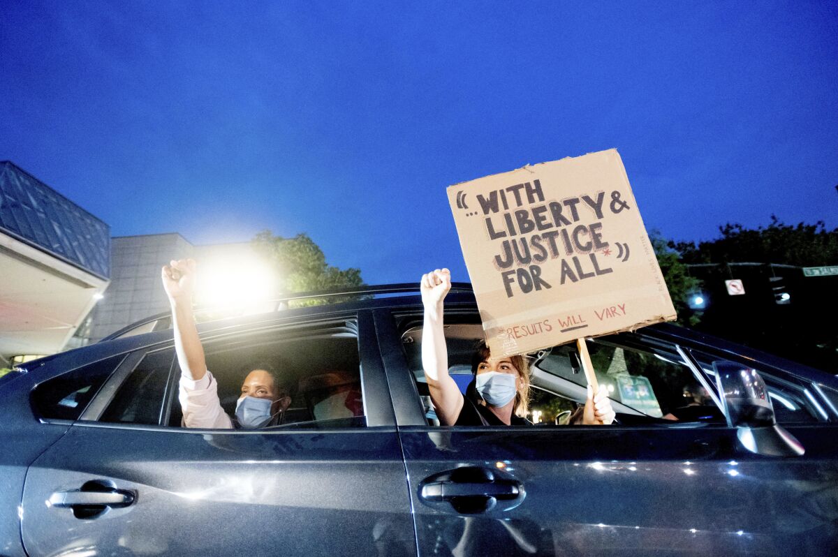 Bobbi Snethen, right, holds a sign during a protest caravan for Black Lives Matter on Friday, July 31, 2020, in Portland, Ore. Following an agreement between Democratic Gov. Kate Brown and the Trump administration to reduce federal officers in the city, nightly protests remained largely peaceful without major confrontations between demonstrators and officers. (AP Photo/Noah Berger)