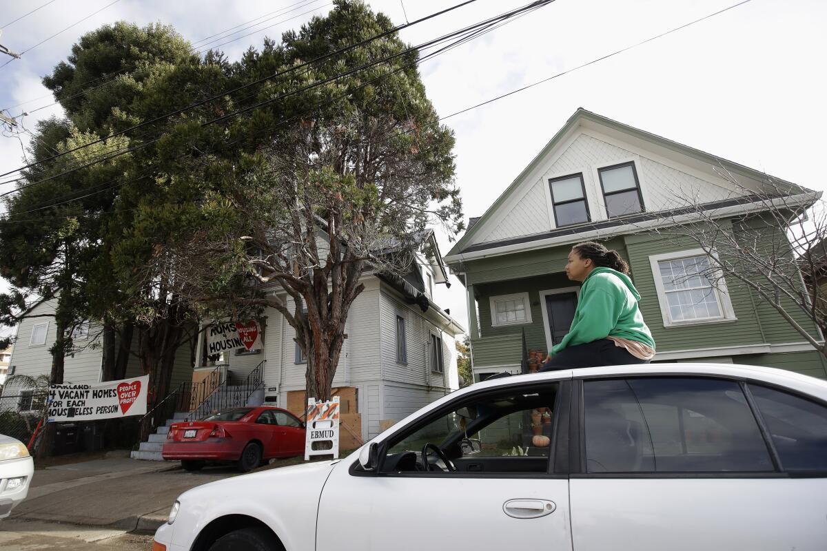 Sunday Simon, a supporter of homeless women who were occupying a house, sits on a car near the house, at left, in Oakland.
