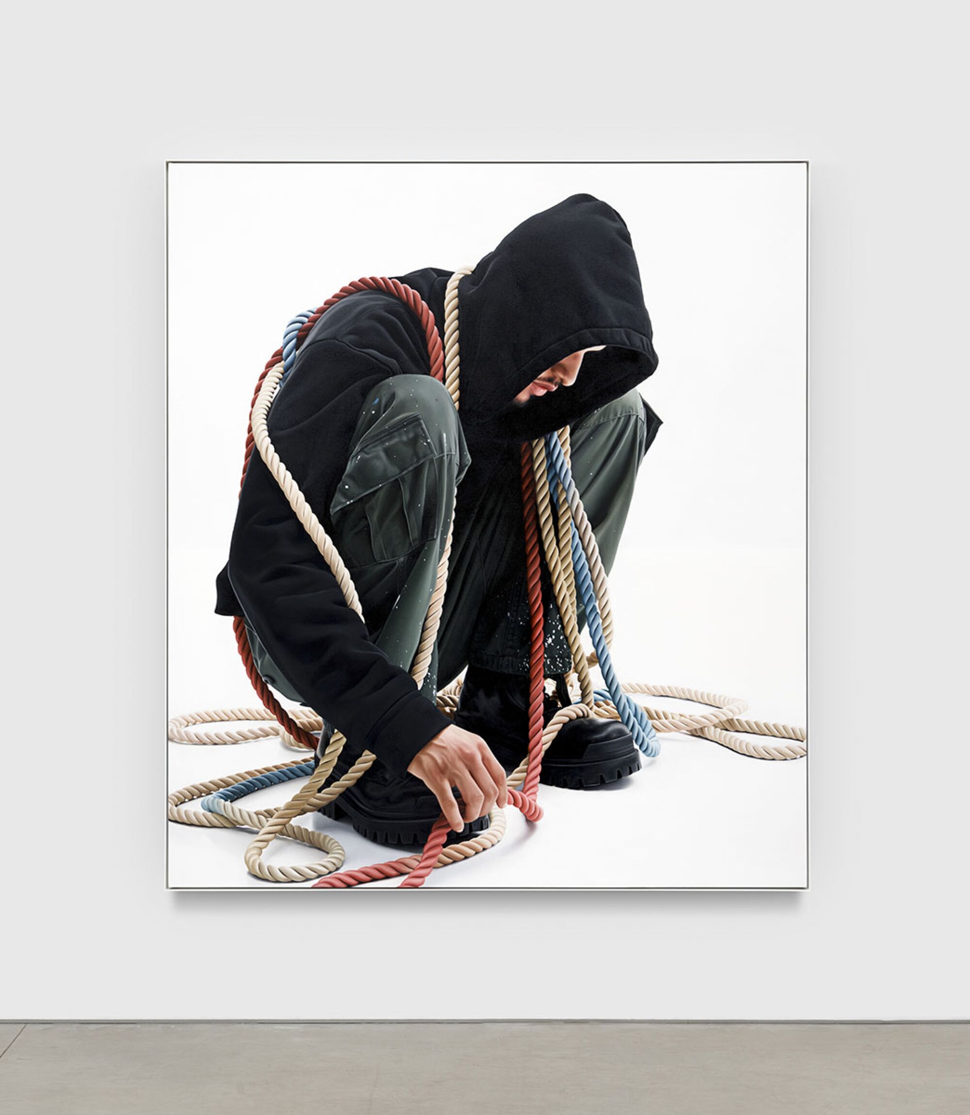 A crouching figure is draped with ropes