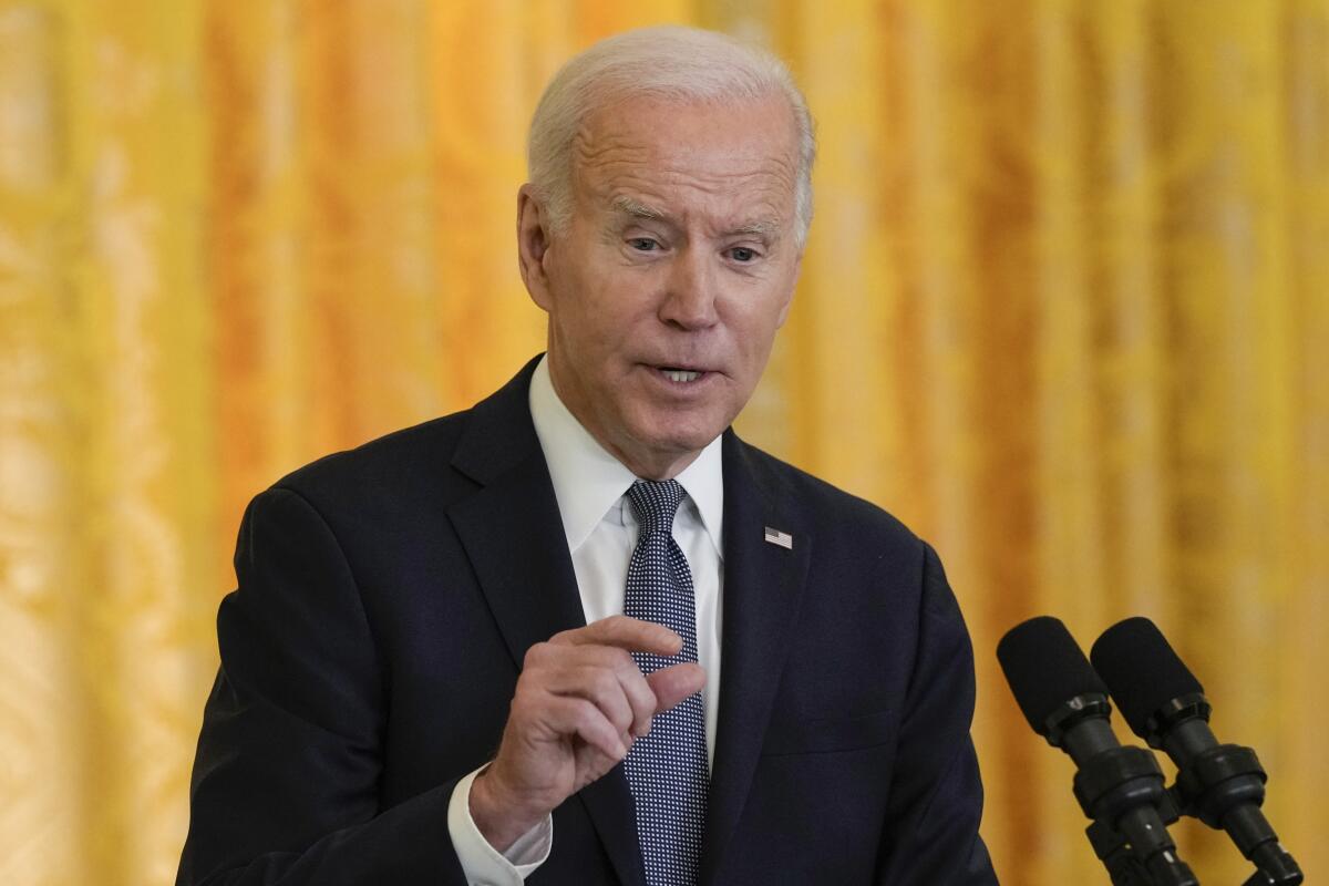 President Biden gestures with his right hand as he speaks into microphones at a news conference inside the White House.