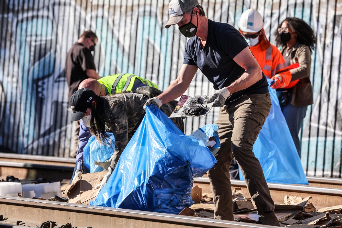 Gov. Gavin Newsom helps clean debris from train tracks on Thursday where cargo cars were looted.