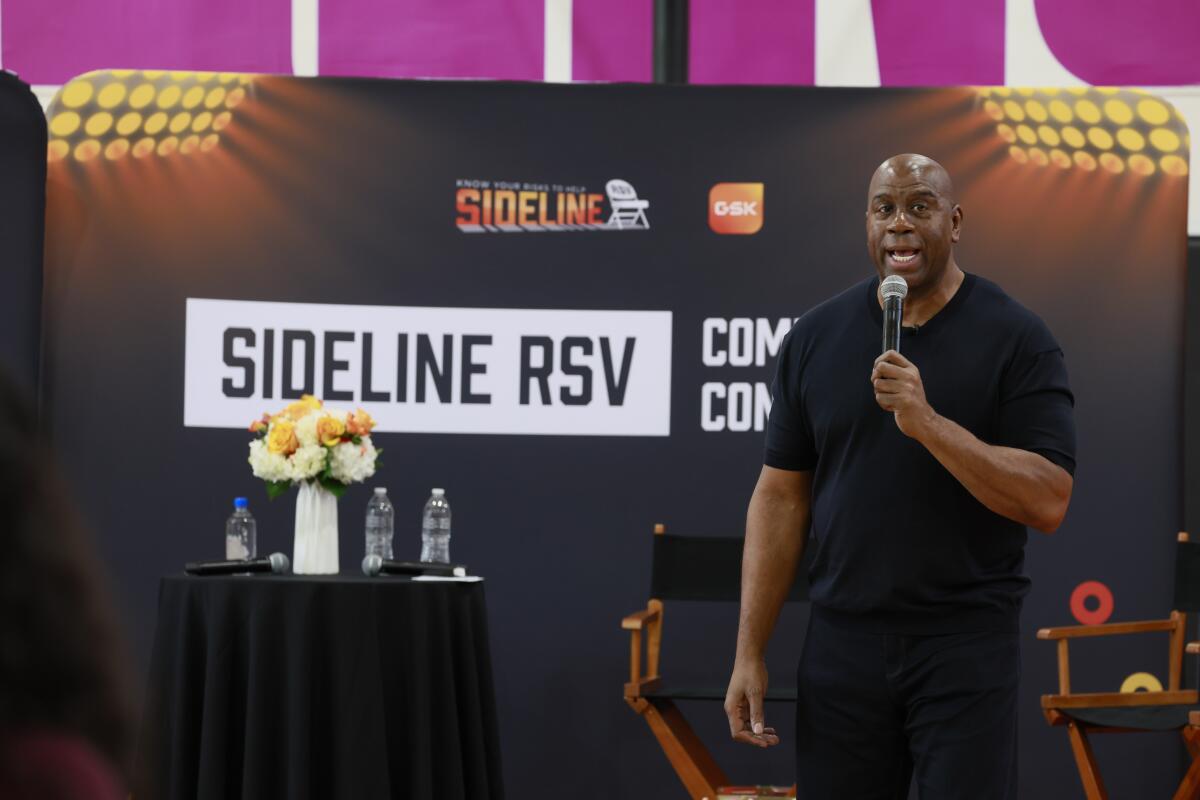 Magic Johnson speaks at the Crenshaw Family YMCA while standing in front of a "Sideline RSV" banner.