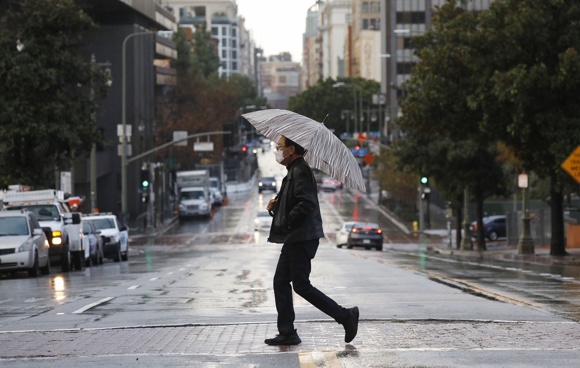 Keith Kim crosses Broadway with umbrella in hand in downtown Los Angeles