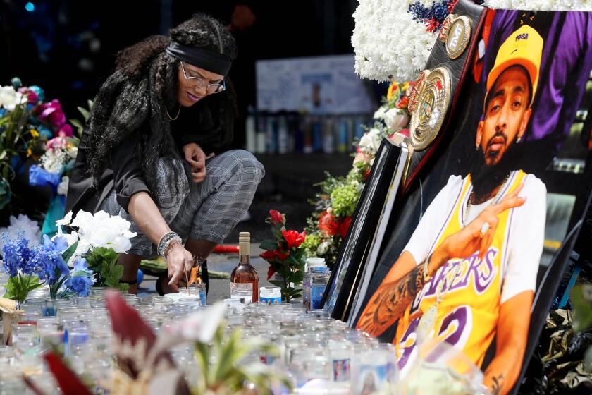 LOS ANGELES, CALIF. -- THURSDAY, APRIL 11, 2019: Corina Samarco, of Ypsilanti, Michigan, pays respect lighting a candle in the parking lot of the Marathon Clothing Company before the start of the Nipsey Hussle Celebration of Life procession in Los Angeles, Calif., on April 11, 2019. (Gary Coronado / Los Angeles Times)