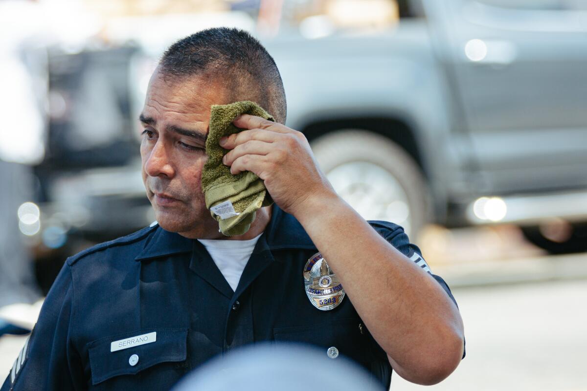 A police officer wipes his face with a rag.