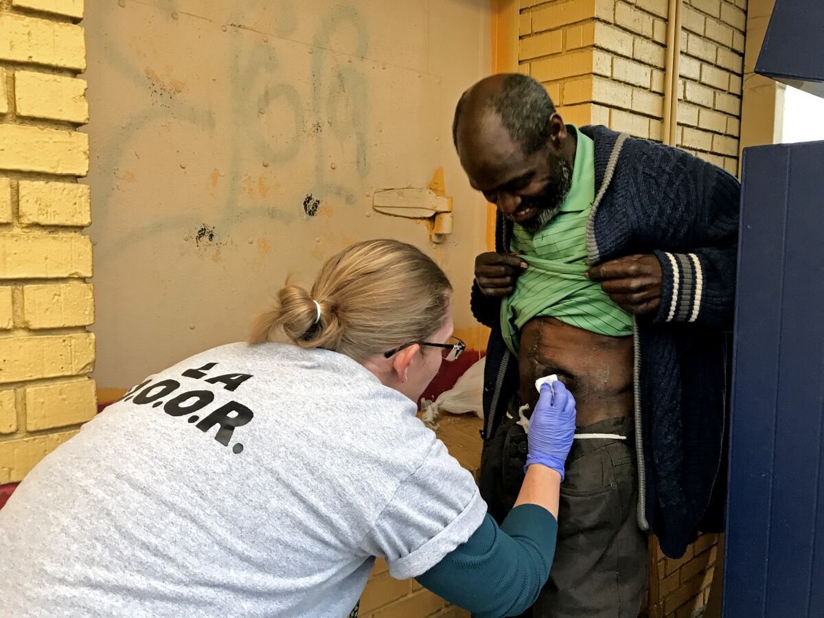 Nurse Sarah Grove helps a client known as Midnight with a wound on his abdomen near his sleeping place behind a Church's Chicken in South L.A.