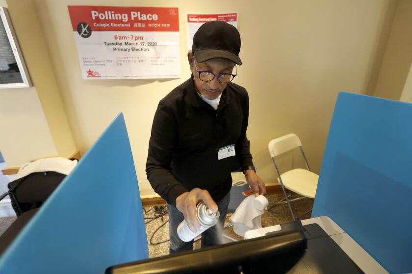 John Davis, a polling judge volunteer, sanitizes an electronic voting machine screen amid concerns about the COVID-19 coronavirus at a polling place in the Bronzeville neighborhood of Chicago, Tuesday, March 17, 2020.