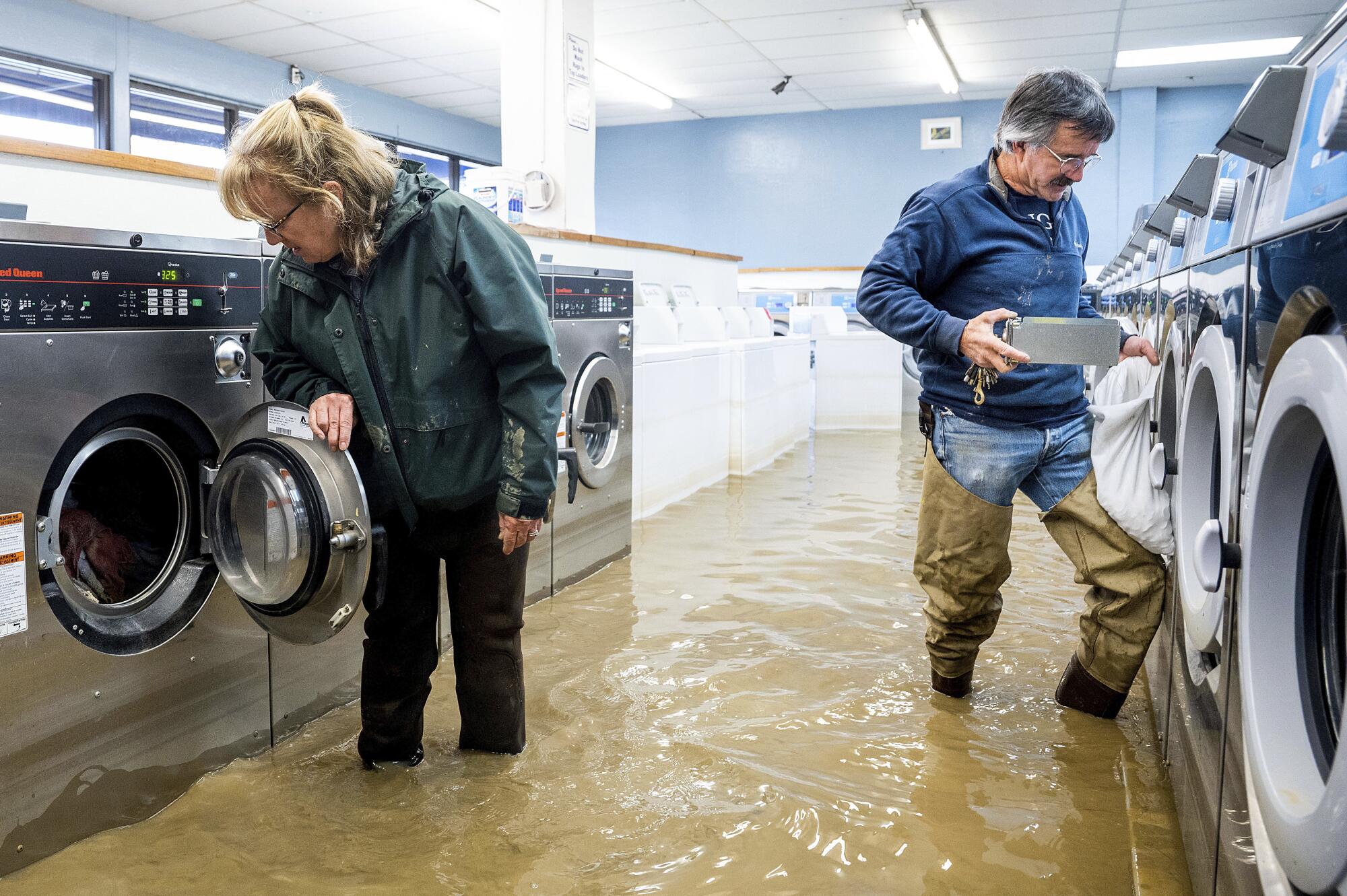 A man and woman empty coins from machines in a flooded  laundromat
