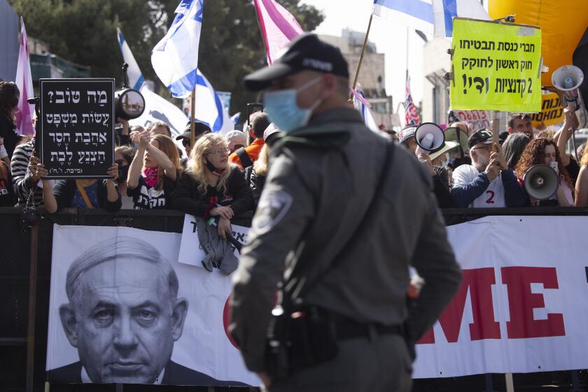 A police officer stands guard in front of protesters as Prime Minister Benjamin Netanyahu's motorcade arrives at the District Court in Jerusalem for a hearing in his corruption trial, Monday, April 5, 2021. Netanyahu was back in court for his corruption trial on Monday as the country's political parties were set to weigh in on whether he should form the next government after a closely divided election or step down to focus on his legal woes. (AP Photo/Maya Alleruzzo)