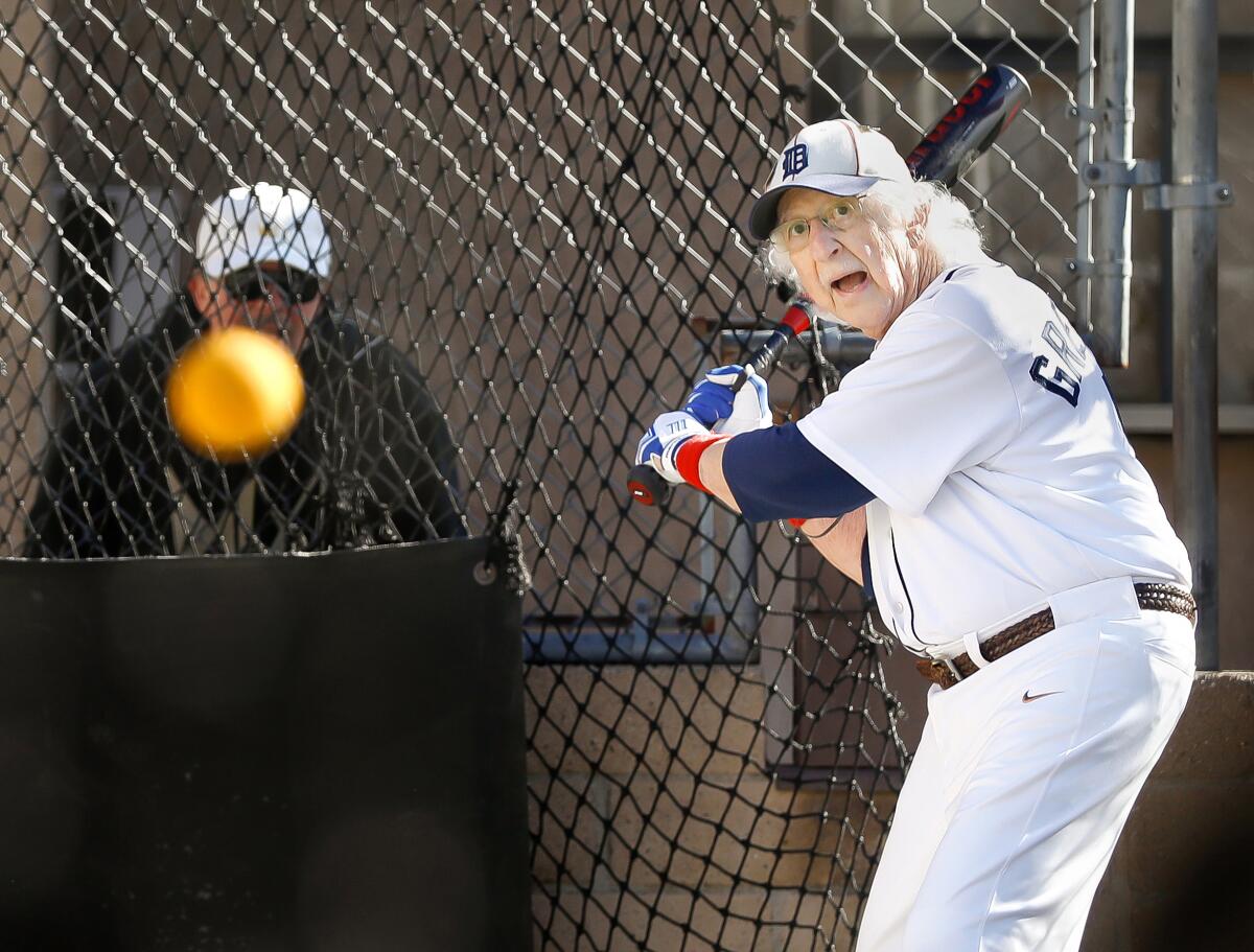 A man in a baseball outfit holds a bat as an orange ball flies toward him.