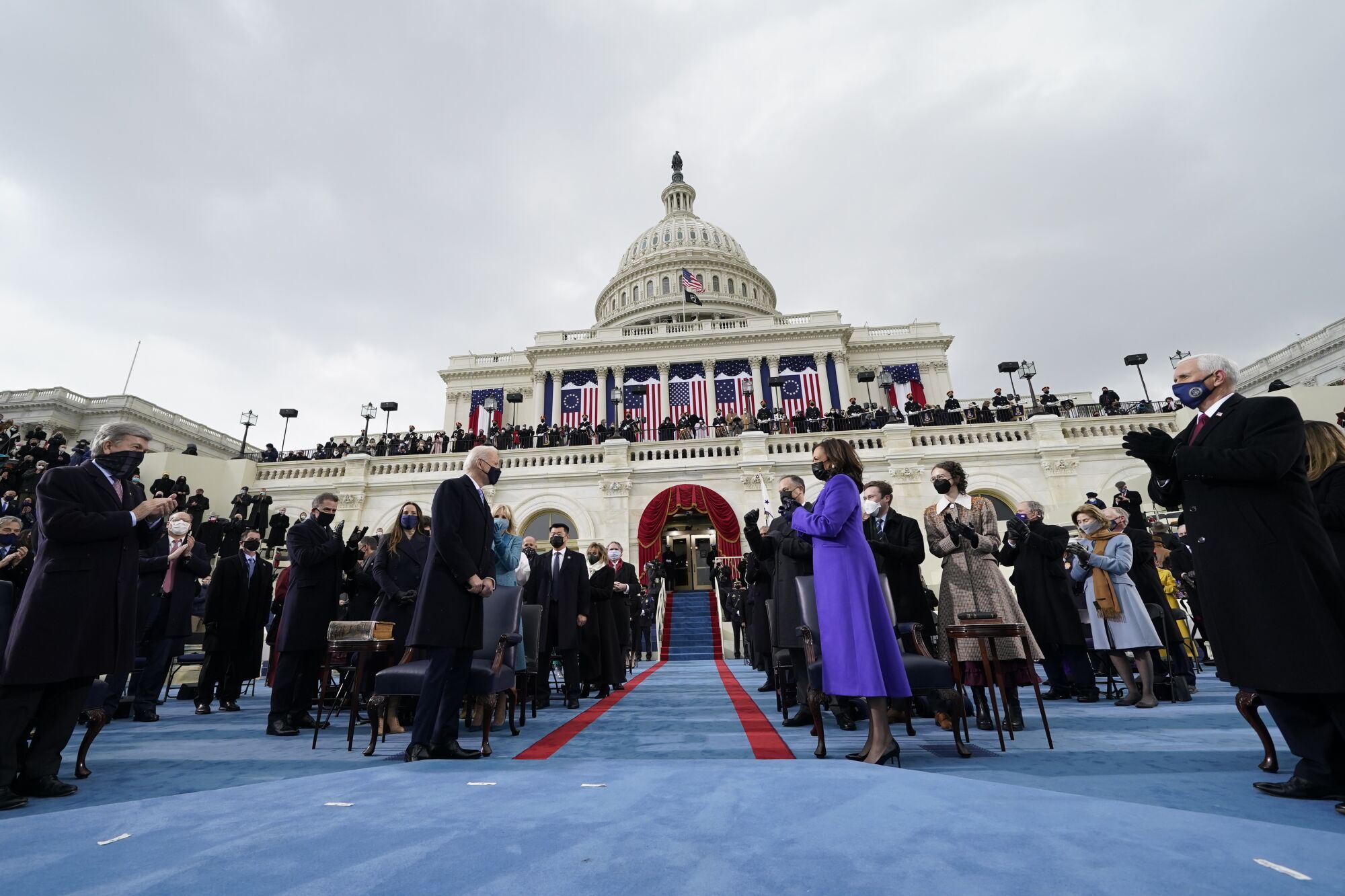 Kamala Harris applauds as Joe Biden arrives for his inauguration with people and the U.S. Capitol in the background.