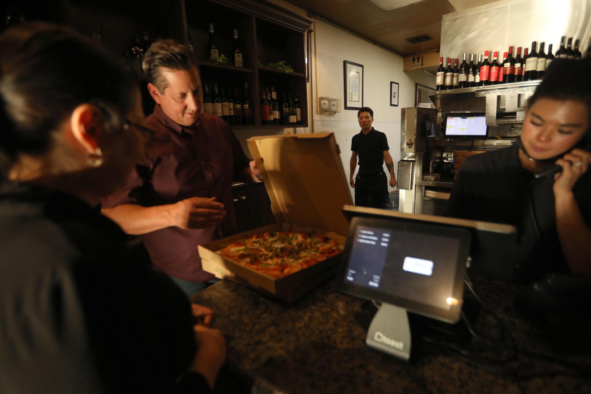 Louise's Trattoria co-owner Rob Serritella, second from left, displays a pizza