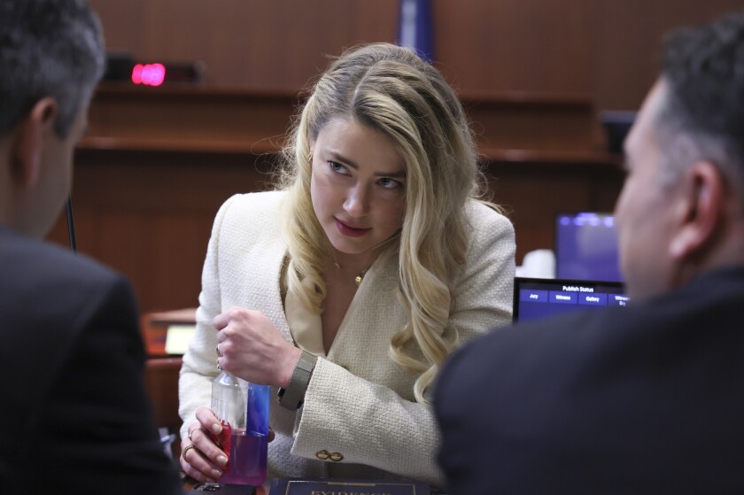 A blond woman talks to two attorneys in a Virginia courtroom.