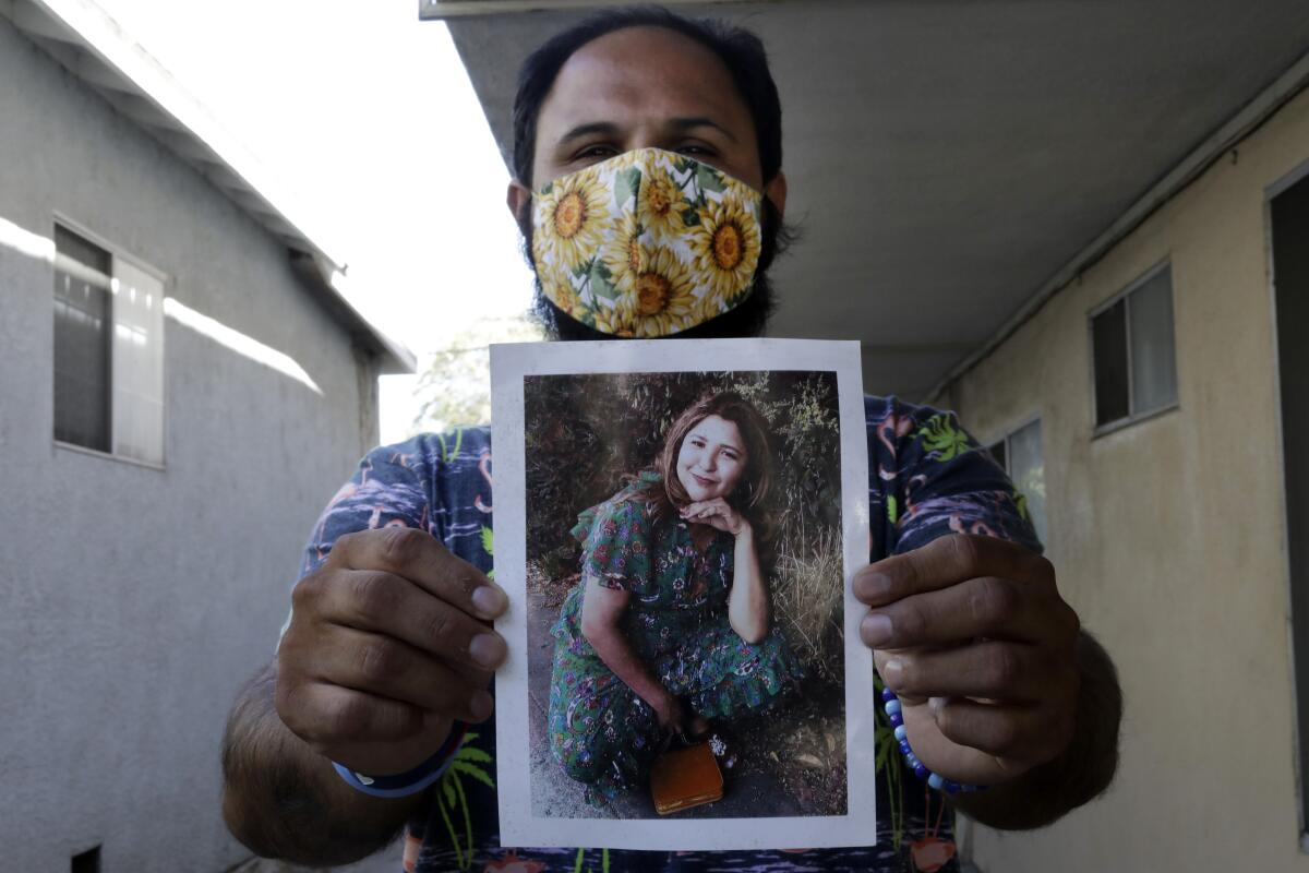 A man holds up a photo of his sister, who was killed by the LAPD at the Trader Joe's store where she worked.