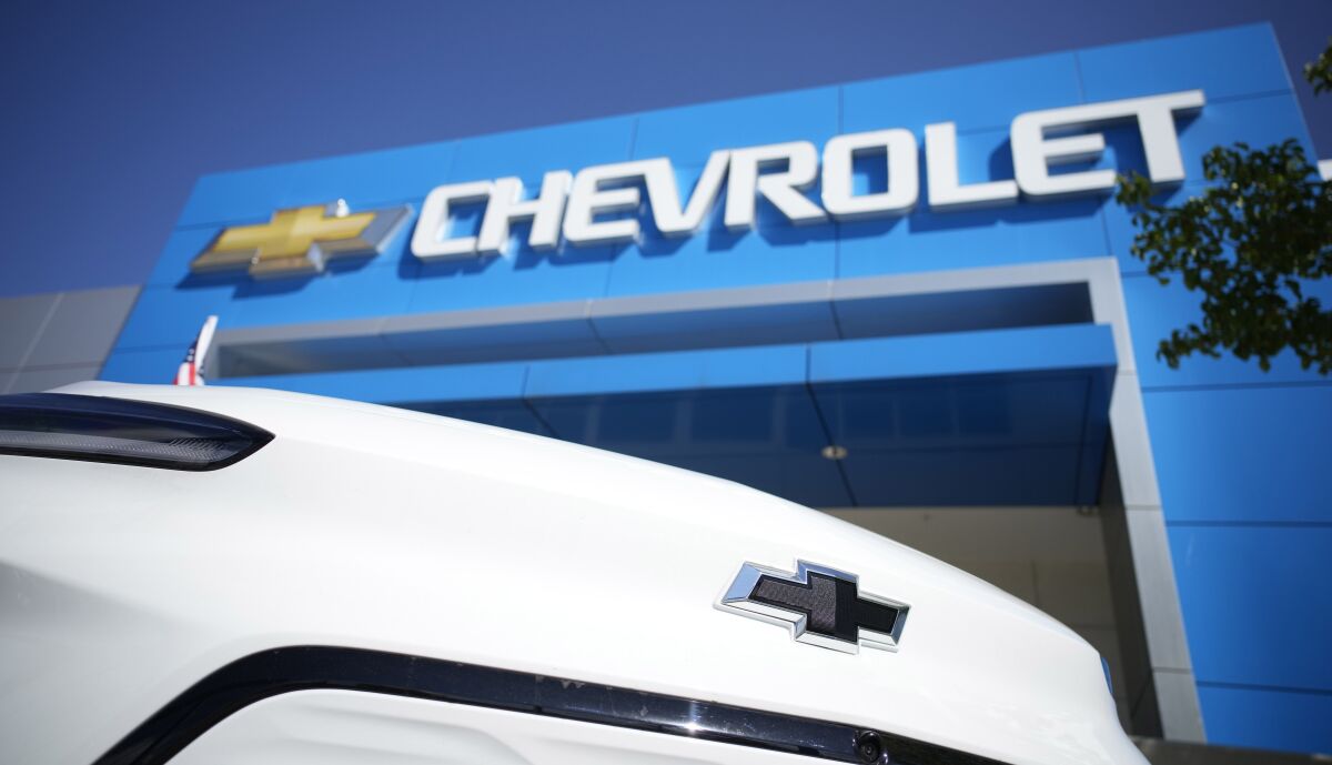 FILE - The company logo shines off the nose of an unsold Bolt electric vehicle on display in front of a Chevrolet dealership Sunday, Sept. 12, 2021, in Englewood, Colo. General Motors says it will start making Chevrolet Bolt electric vehicles again in early April after an eight-month pause due to a series of battery fire recalls. The automaker says Tuesday, Feb. 15, 2022, that battery supplier LG Energy Solution is now making enough to supply replacement modules for the recalls as well as to resume production. (AP Photo/David Zalubowski)