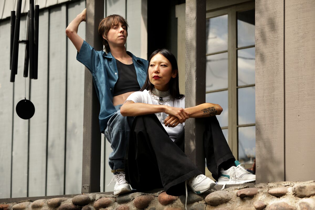 A trans musician and a female musician seated in front of a house