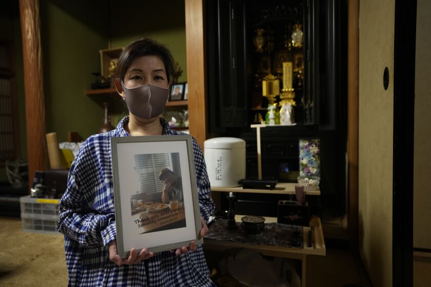 Kaori Takada poses with her brother's photo in front of her family altar at her home in Matsubara, south of Osaka, western Japan, Tuesday, Nov. 16, 2021. Takada and another woman whose family member died at home while sick with the coronavirus have formed a group to protest the Japanese government's policy of having infected people recuperate at home. Takada's brother was diagnosed with the coronavirus this year. When he didn't answer calls from public health workers for three days, police went to his home and found him dead in his bed. He was 43. (AP Photo/Hiro Komae)