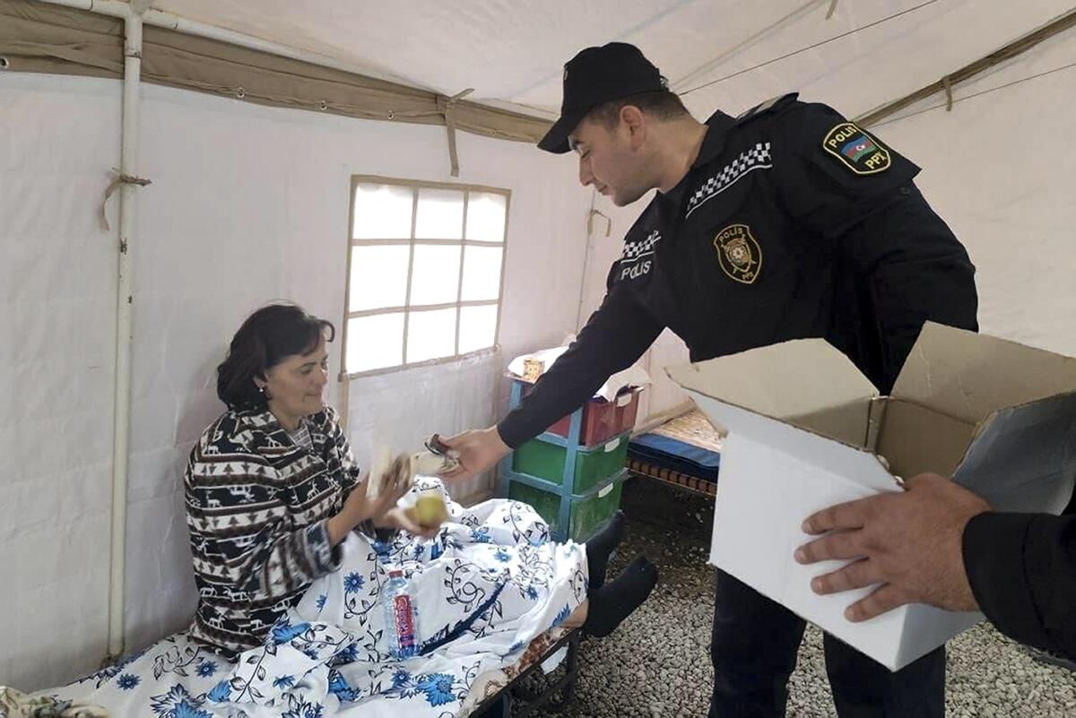 An Azerbaijani police officer gives food to an ethnic Armenian woman sitting in a tent.