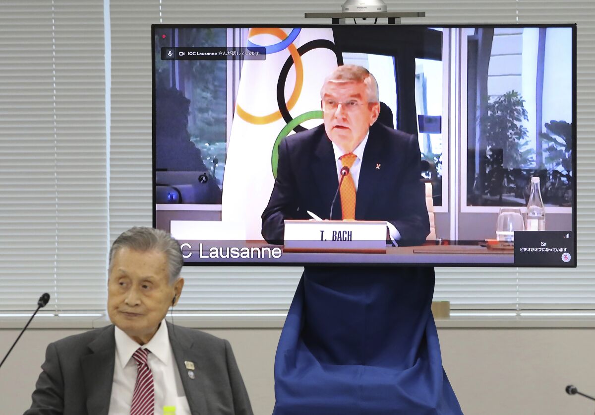 In this Sept. 24, 2020, file photo, IOC President Thomas Bach, on the screen, speaks remotely with Tokyo 2020 Organizing Committee President Yoshiro Mori, left, during an online meeting focused on how to pull off the delayed Tokyo Games, in Tokyo. Tokyo Olympic organizers estimate they have found saving of about $280 million by simplifying and cutting out some frills from next year's postponed Games. (Du Xiaoyi/Pool Photo via AP, File)