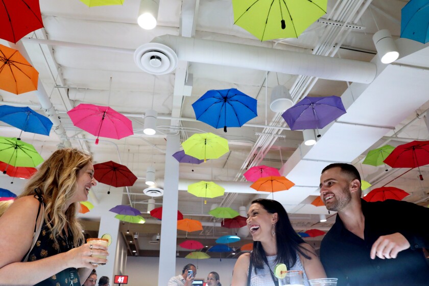 Three people standing beneath colorful umbrellas hanging from a ceiling.