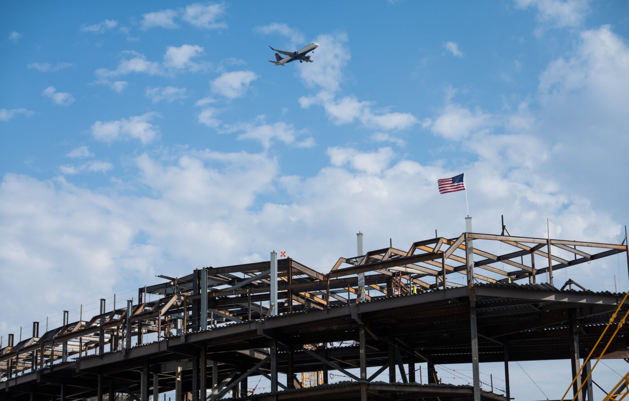 A plane flying into LAX soars over the rising Intuit Dome construction site.