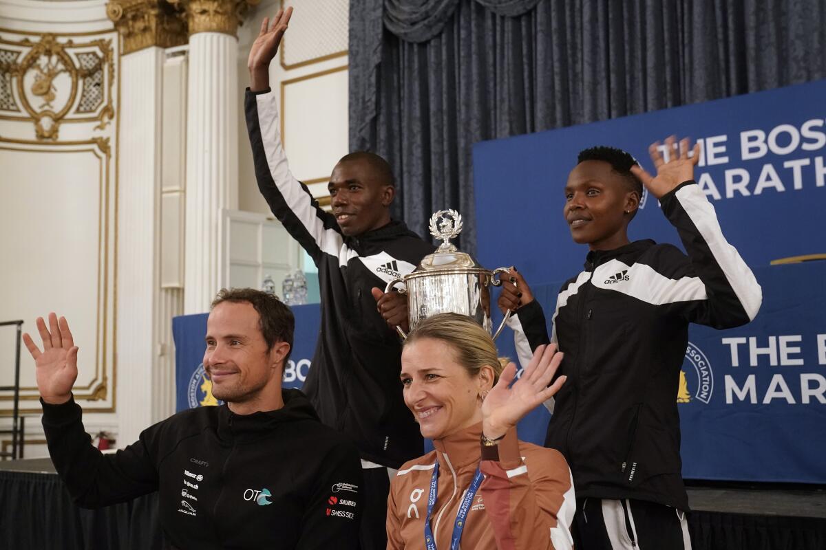 Marcel Hug, front left, Manuela Schar, front right, both of Switzerland, and Benson Kipruto, rear left, and Diana Kipyokei, rear right, both of Kenya, wave while posing for a photograph following a news conference, Tuesday, Oct. 12, 2021, in Boston. Hug and Schar won the men's and women's wheelchair races, while Kipruto and Kipyokei won the men's and women's foot race in the pandemic-delayed Boston Marathon, Monday, Oct. 11, when the race returned from a 30-month absence with a smaller, socially distanced feel and moved from the spring for the first time in its 125-year history. (AP Photo/Steven Senne)