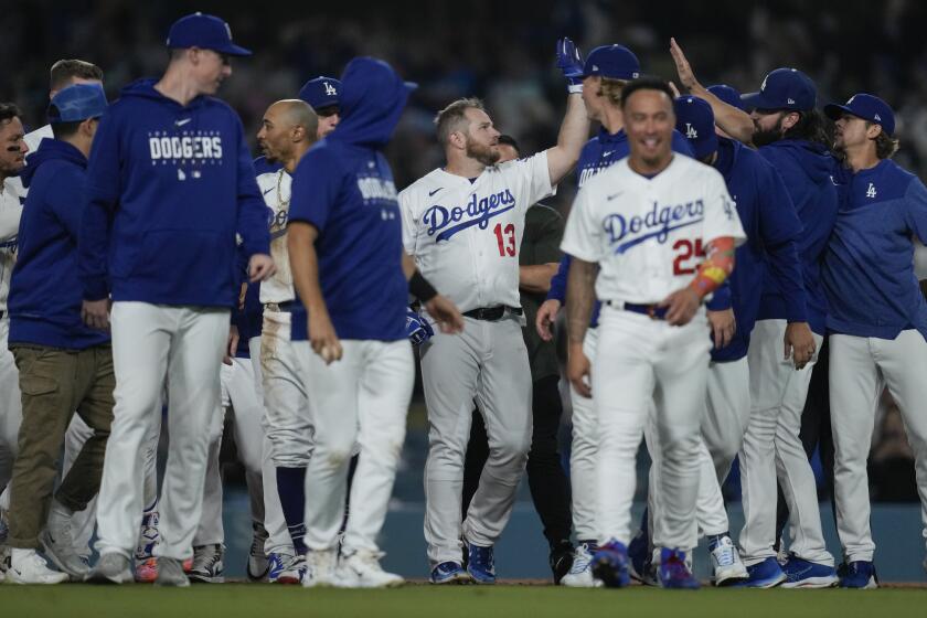 Max Muncy is surrounded by teammates on the field and reaches out for a high five after hitting a walk-off single