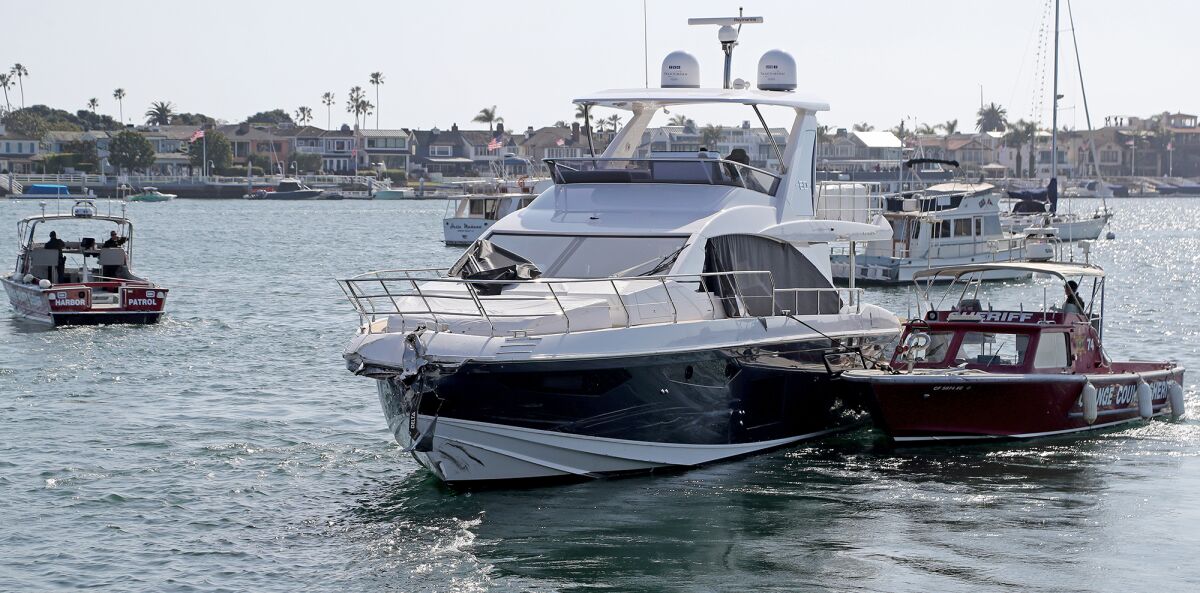 A yacht with damage to its front end is pulled by a sheriff tugboat