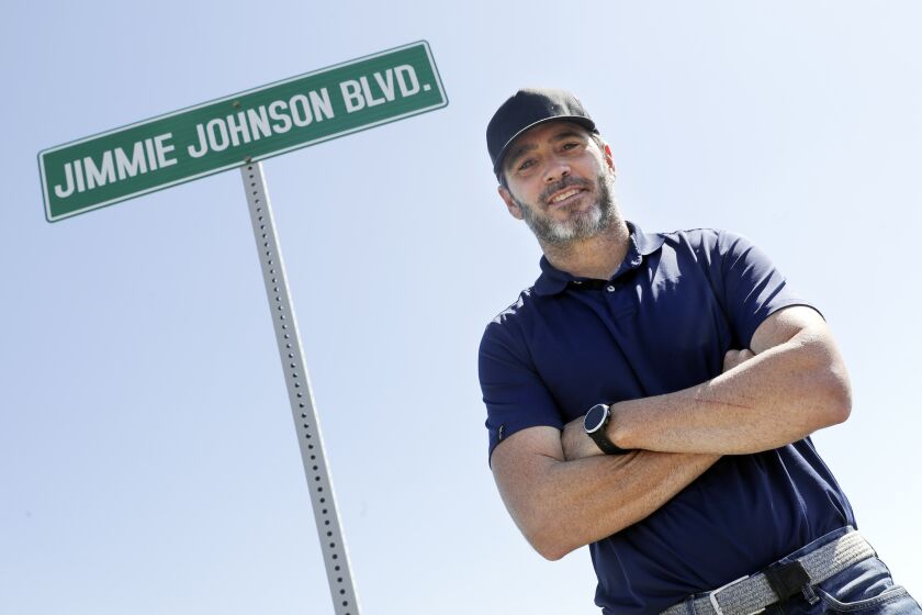 FILE - Driver Jimmie Johnson poses in front of a street sign after the street was named for him outside Kentucky Speedway before a NASCAR Cup Series auto race Sunday, July 12, 2020, in Sparta, Ky. The Seven-time NASCAR champion is retiring from full-time racing and will turn his focus toward spending time with family. He figures his future schedule will include no more than 10 bucket list events and has his sights set on the 24 Hours of Le Mans. (AP Photo/Mark Humphrey, File)