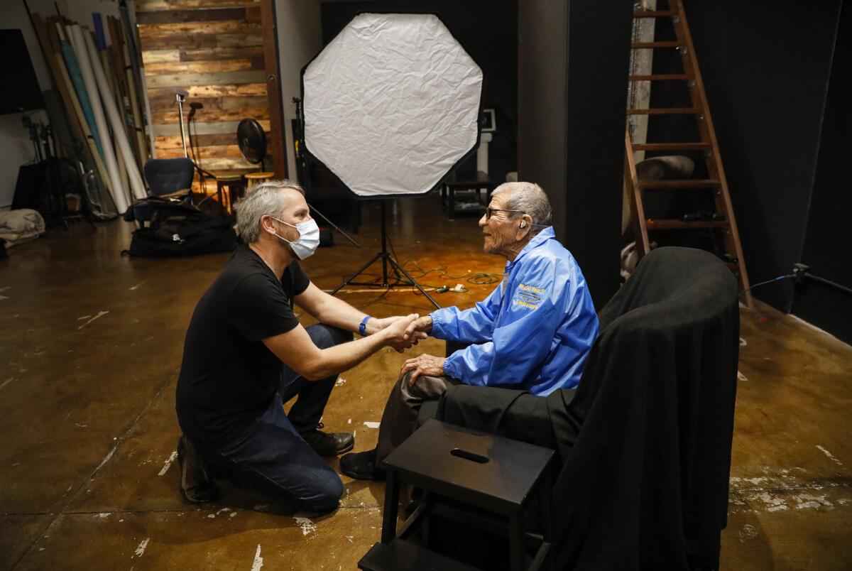 Portrait photographer Mickey Strand, left, greets World War II veteran Joe Albert Gonzalez, 95, at his studio