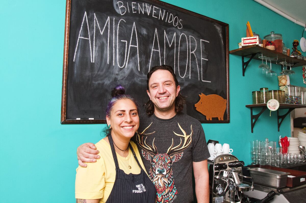 Amiga Amore owners Danielle Duran Zecca and Alessandro Zecca stand in their new Highland Park restaurant against a teal wall.