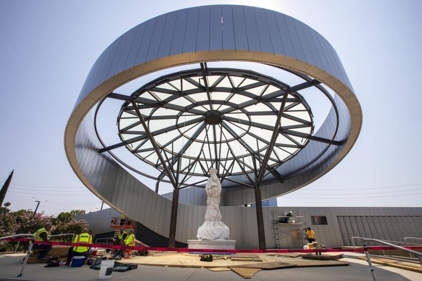 GARDEN GROVE, CA - JULY 12: Workers are putting the finishing touches around the new Our Lady of La Vang Shrine at Christ Cathedral Campus on Monday, July 12, 2021 in Garden Grove, CA. Wrapped in white canvas, the centerpiece of the shrine is a statue of the Virgin Mary as she is believed to have appeared before a group of persecuted Vietnamese Catholics in 1798. The carved Italian white marble statue of Our Lady of Vang stands 12 feet tall and weighs an estimated 16,000 pounds. The statue will be unveiled this weekend. (Francine Orr / Los Angeles Times)