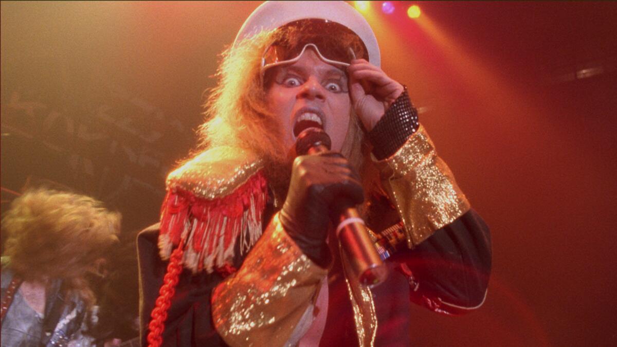 A glam-rock singer scowls and sings into a handheld microphone