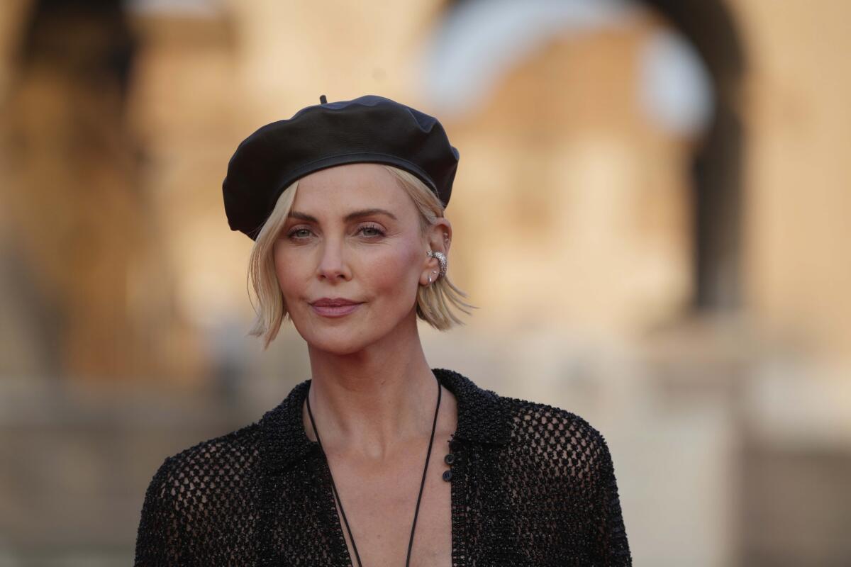 Charlize Theron in a black beret, a sheer black jacket and a long necklace