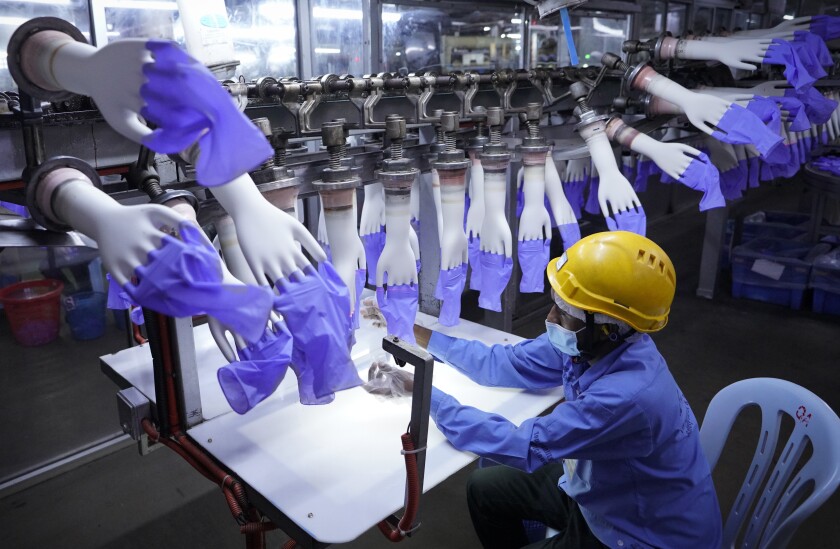 FILE - In this Aug. 26, 2020, file photo, a worker inspects disposable gloves at the Top Glove factory in Shah Alam on the outskirts of Kuala Lumpur, Malaysia. Malaysia's Top Glove Corp., the world's largest rubber glove maker, said Wednesday, May 5, 2021, it hopes to swiftly end a U.S. ban on its products due to allegations of forced labor after one of its shipment was seized at a U.S. port. (AP Photo/Vincent Thian, File)