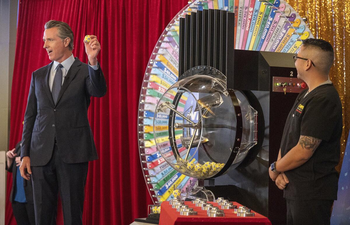 California Gov. Gavin Newsom holds a lottery ball while Claudio Alvarado looks on near a wheel of fortune