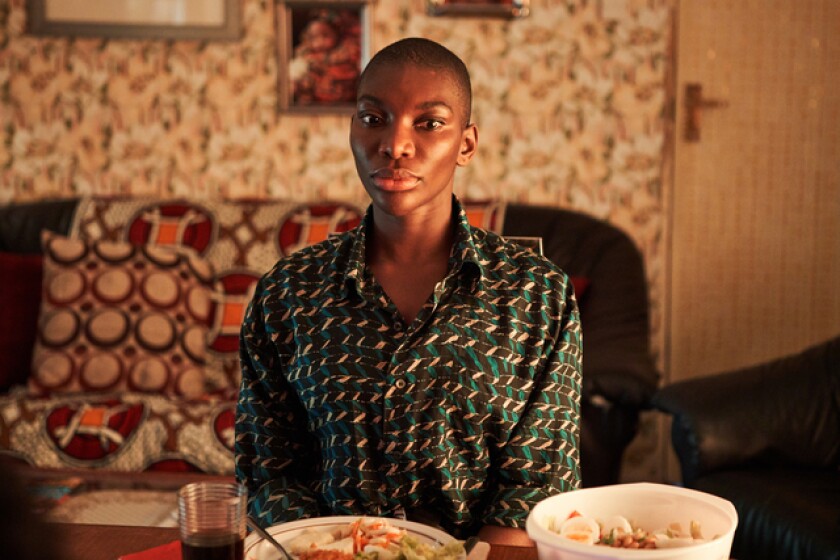 A seated woman in a green patterned blouse looks at the camera.