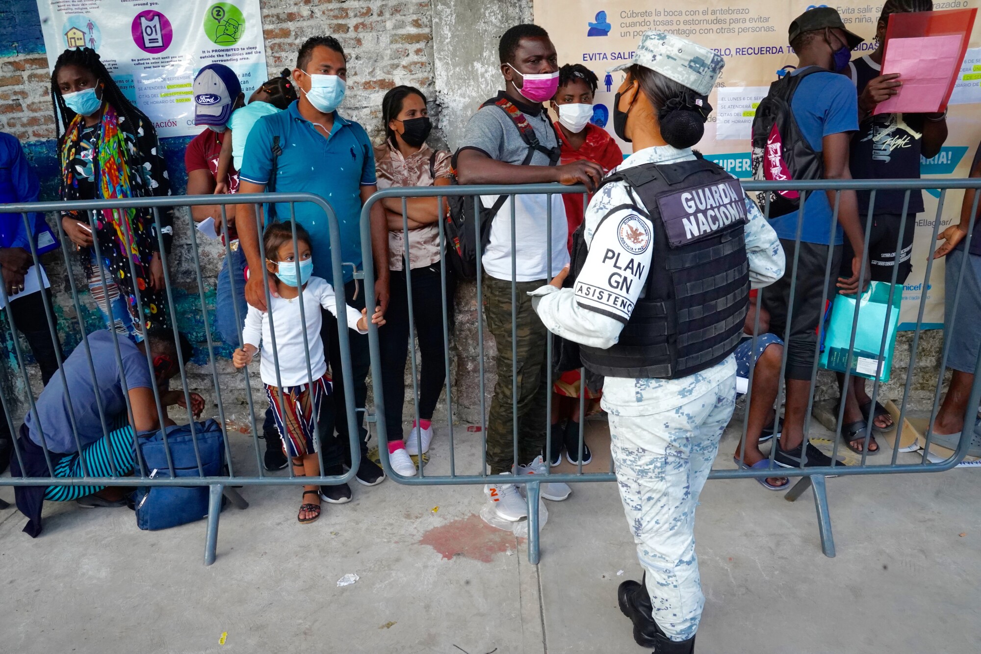 A national guard member watches over people in line along a brick wall. 