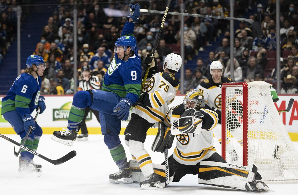 Boston Bruins defenseman Connor Clifton (75) tries to clear Vancouver Canucks center J.T. Miller (9) from in front of Bruins goaltender Jeremy Swayman (1) during the second period of an NHL hockey game Wednesday, Dec. 8, 2021 in Vancouver, British, Columbia. (Jonathan Hayward/The Canadian Press via AP)