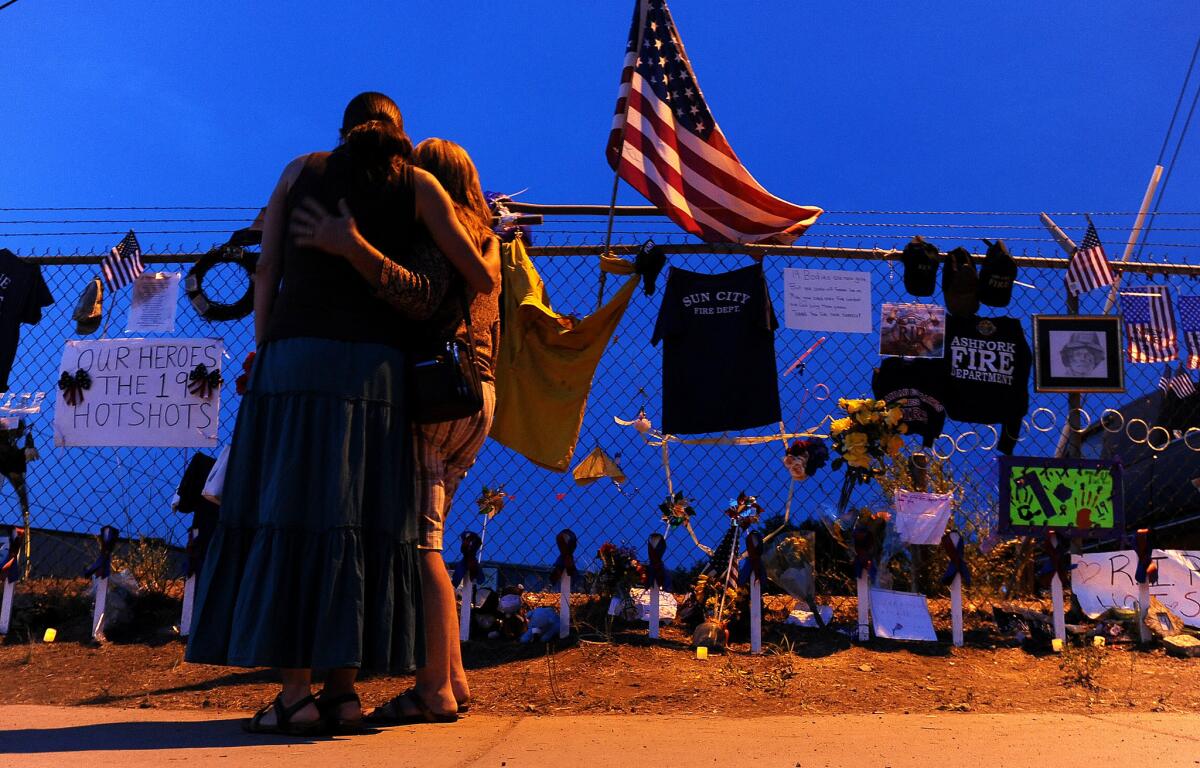 Two women console each other as they stand in front of a memorial in Prescott, Ariz. for the 19 firefighters killed.