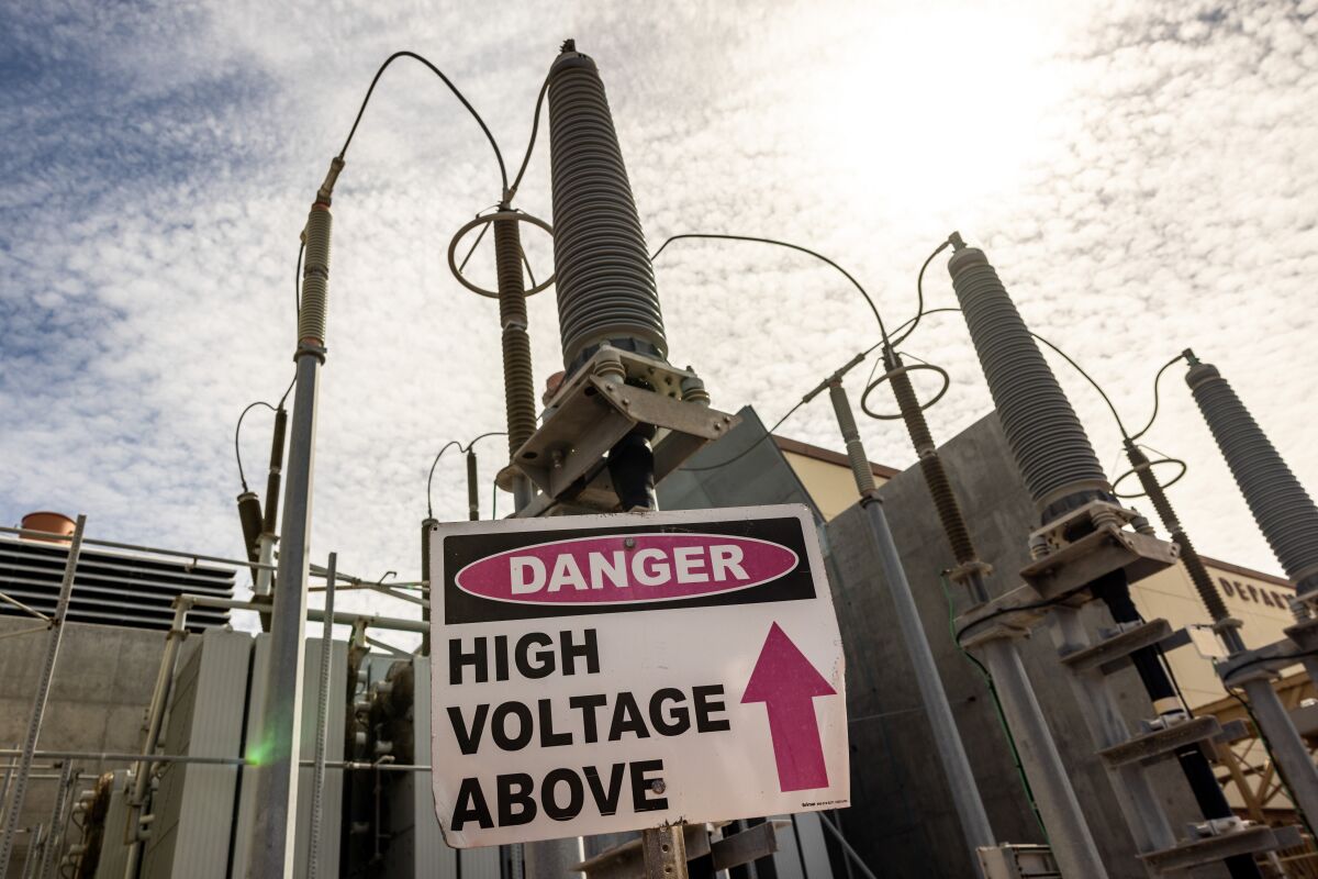 A sign warns "danger high voltage above" among power lines and cooling towers.