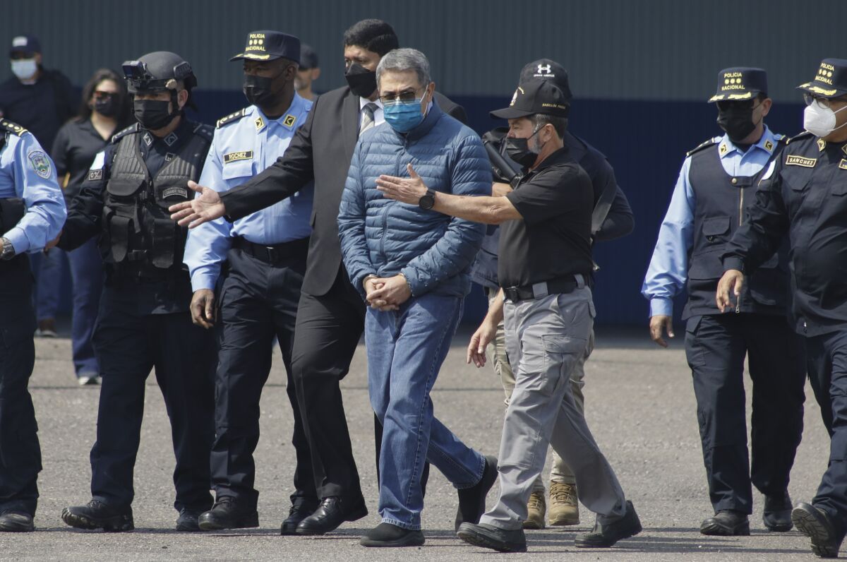 El expresidente hondureño Juan Orlando Hernández, centro, es llevado esposado a un avión