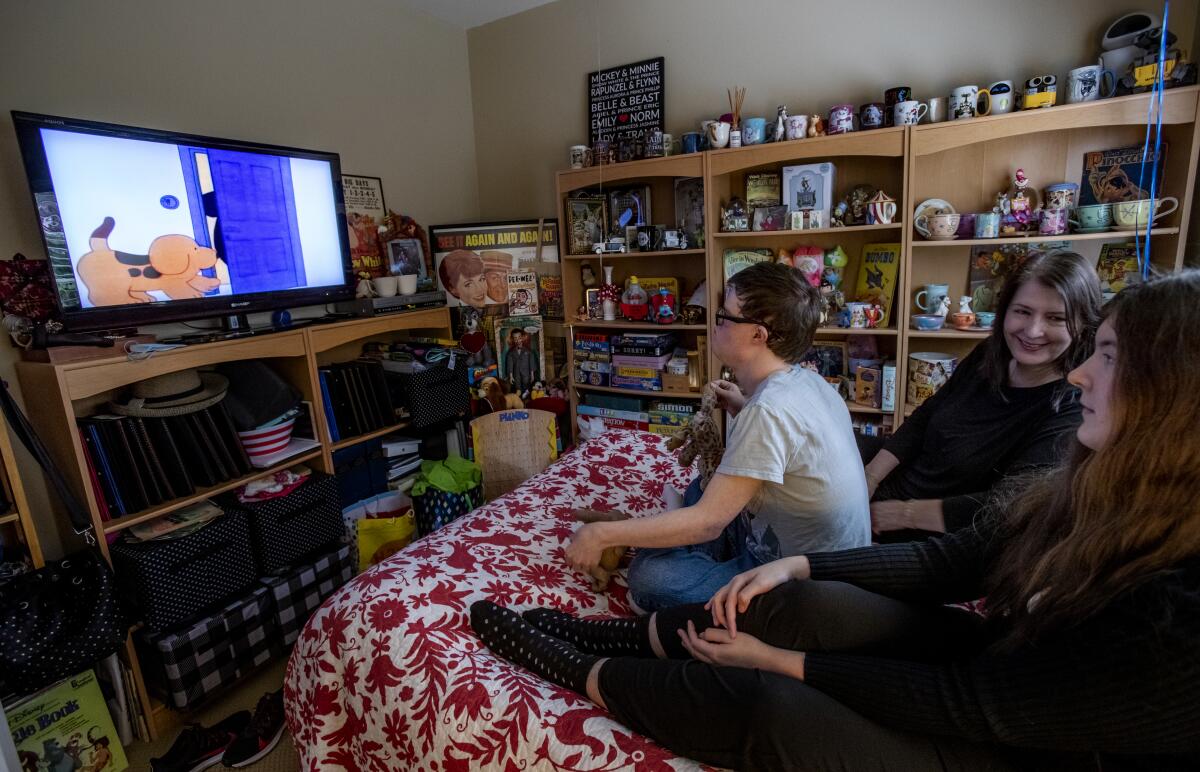 Three people sit on a bed and watch TV