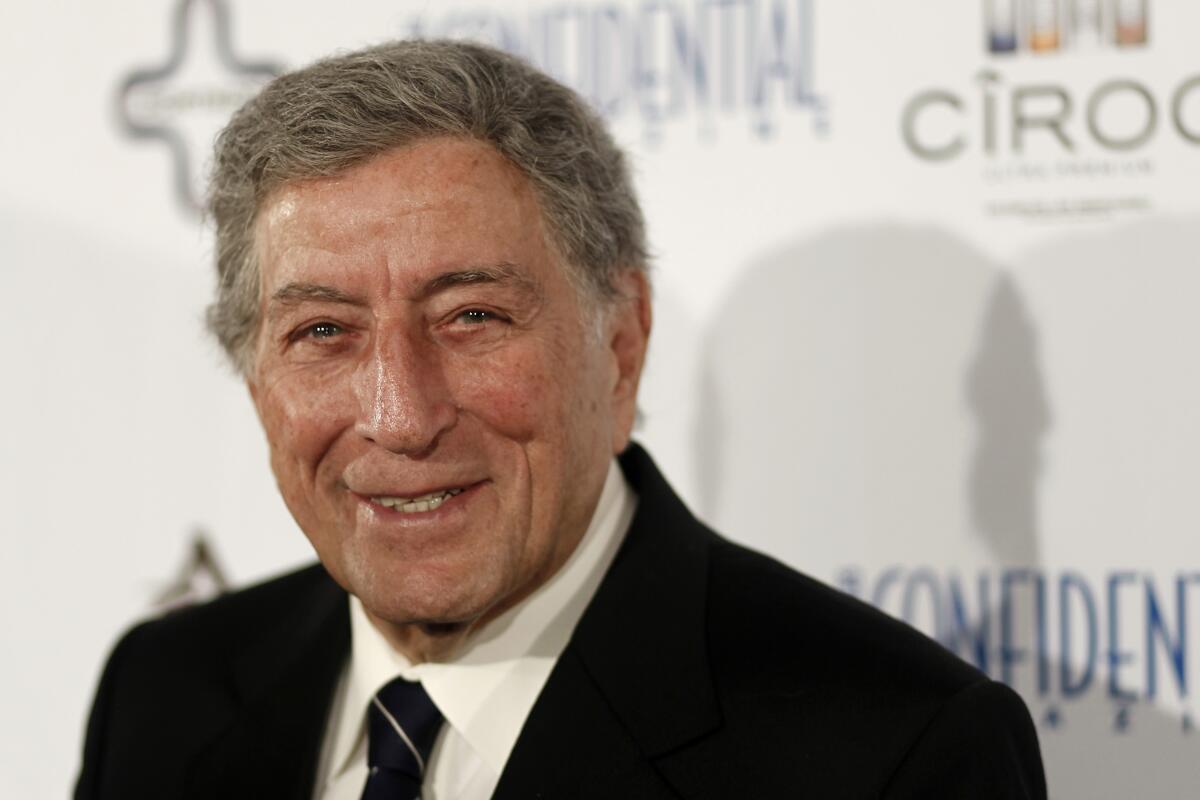 Tony Bennett poses in a black blazer with a collared shirt and black tie with a silver stripe.