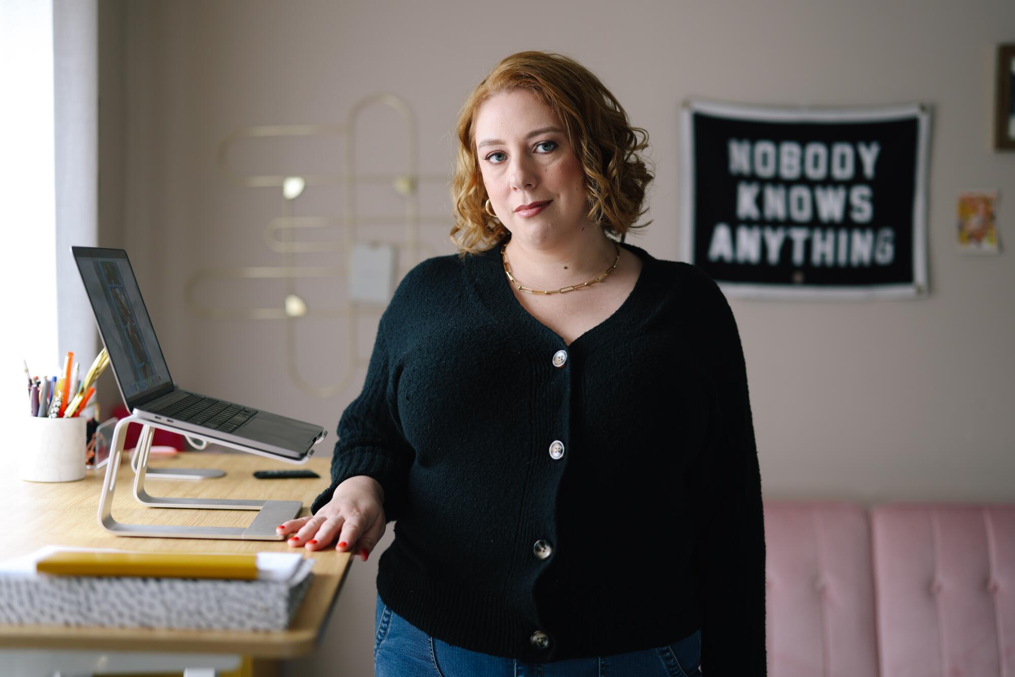 A woman stands in a home office next to a high desk. A banner on the wall behind her says "Nobody knows anything." 