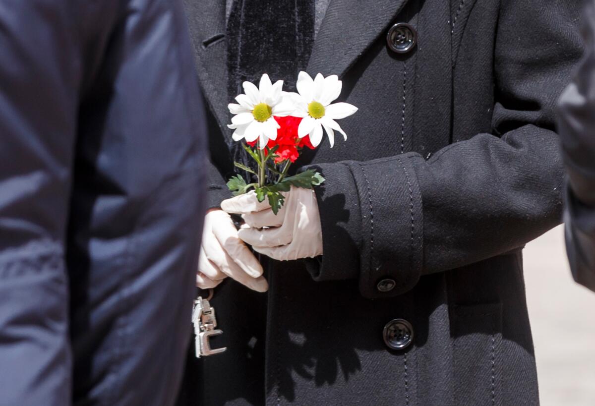 A man wearing gloves holds flowers during the burial service of a man who died of the new coronavirus, at the South Municipal cemetery in Madrid on March 23.